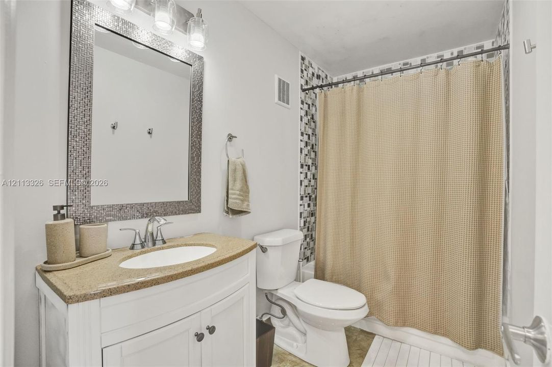 Bathroom featuring a white vanity cabinet with a stone-composite countertop, oval undermount sink, mosaic-tiled mirror frame, and a shower-tub combination with decorative mosaic wall tile