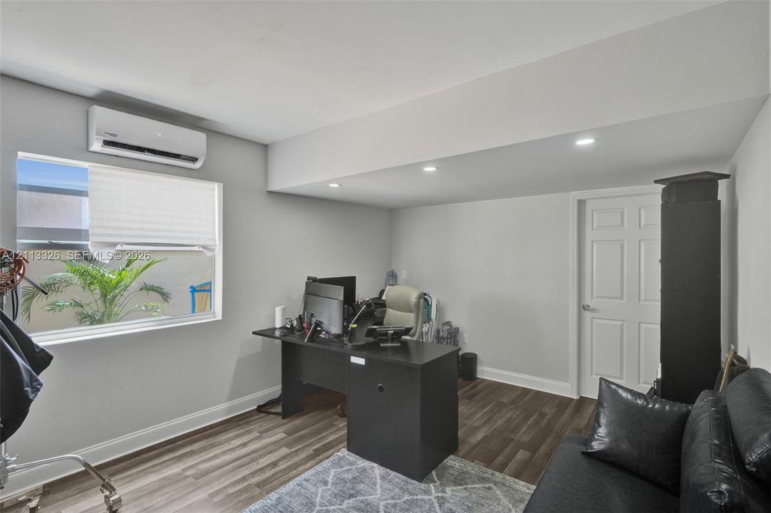 Interior space featuring wood-finish flooring, recessed lighting, a wall-mounted ductless air conditioning unit, and a six-panel door