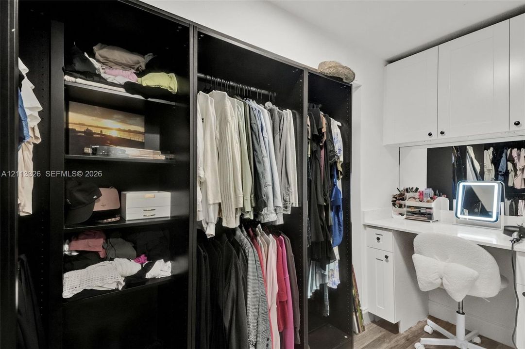 Custom built-in storage system featuring floor-to-ceiling shelving, hanging rods, integrated white cabinetry, and a dedicated vanity station with a countertop