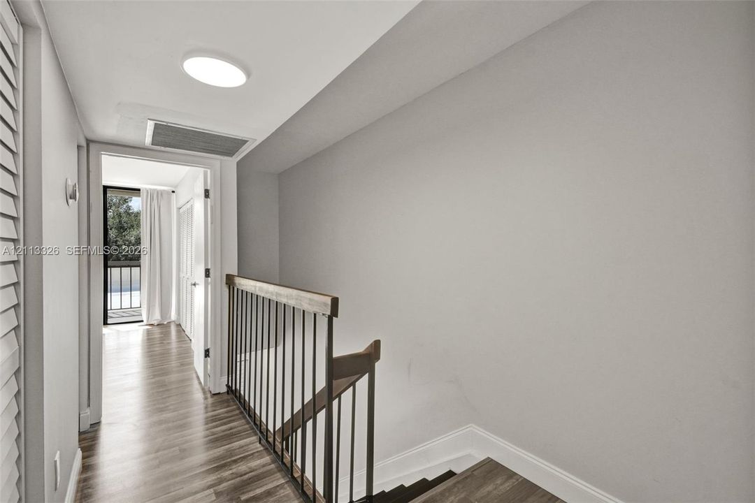 Hallway featuring wood-finish flooring, staircase with a dark metal railing, and ceiling-mounted flush light fixture