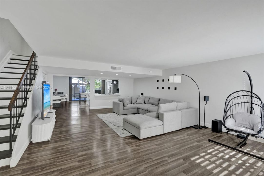 Living area featuring wood-finish flooring, recessed lighting, and a staircase with a black metal railing, accented by a pass-through opening to the interior