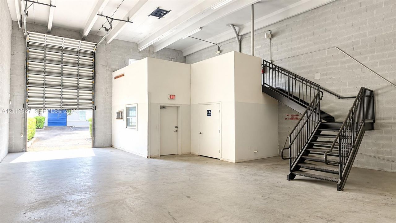 ceilings, a roll-up bay door, exposed masonry walls, and a metal staircase with integrated railing