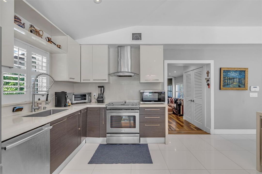 Kitchen featuring two-tone flat-panel cabinetry, quartz countertops, stainless steel appliances, a professional-style pull-down faucet, and polished tile flooring