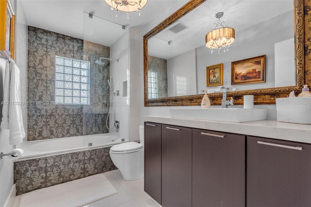 Bathroom featuring a floating vanity with a vessel sink, stone-finish countertop, glass-enclosed shower with a glass block window, and large-format tile surround