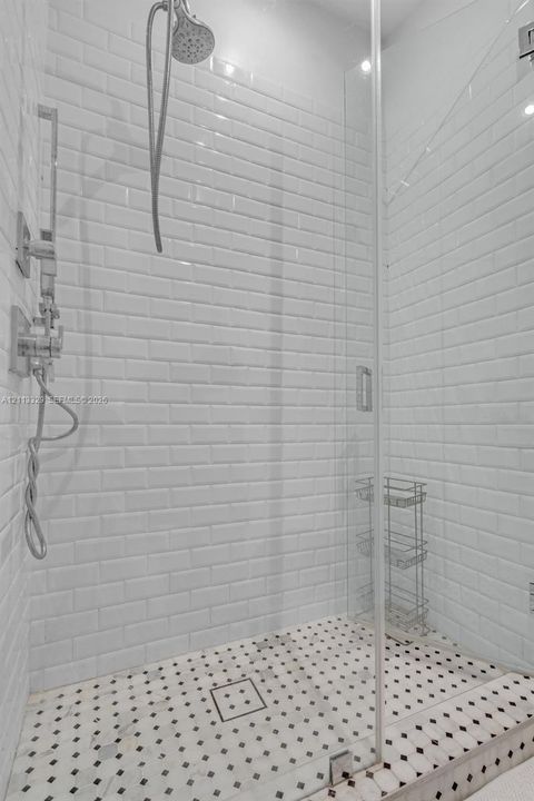 Walk-in shower featuring white subway tile walls, geometric patterned tile flooring, a frameless glass door, and polished chrome plumbing fixtures
