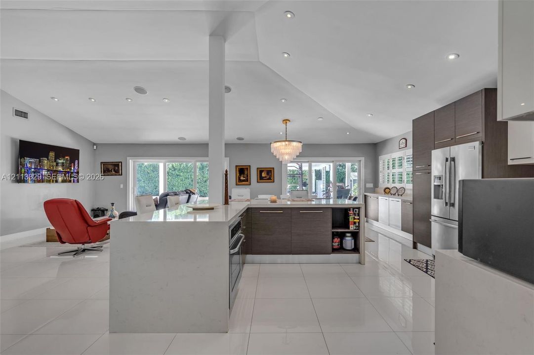 Open-concept kitchen featuring an oversized island with a solid surface countertop, flat-panel cabinetry, recessed ceiling lighting, and porcelain tile flooring