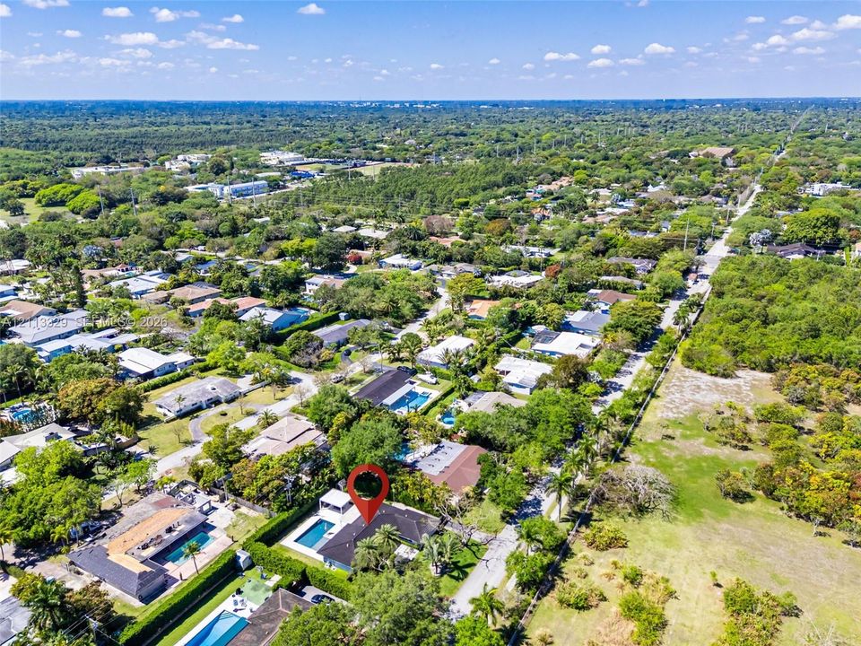 Aerial perspective of a property featuring a swimming pool, covered outdoor area, mature perimeter landscaping, and shingle-style roof