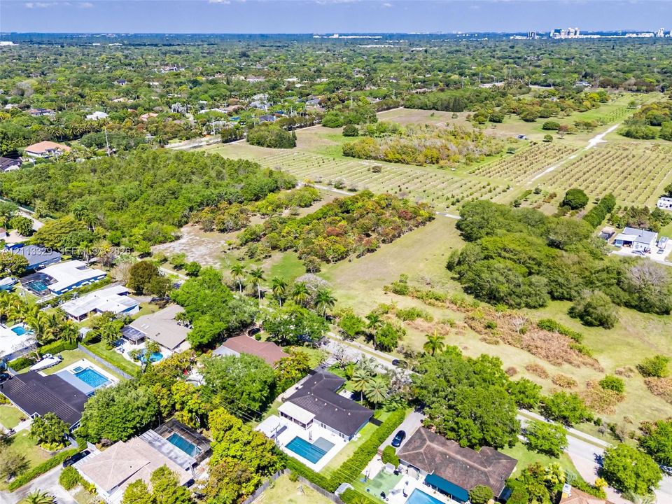 Aerial perspective of expansive residential acreage featuring mature trees, diverse vegetation, and paved access roads