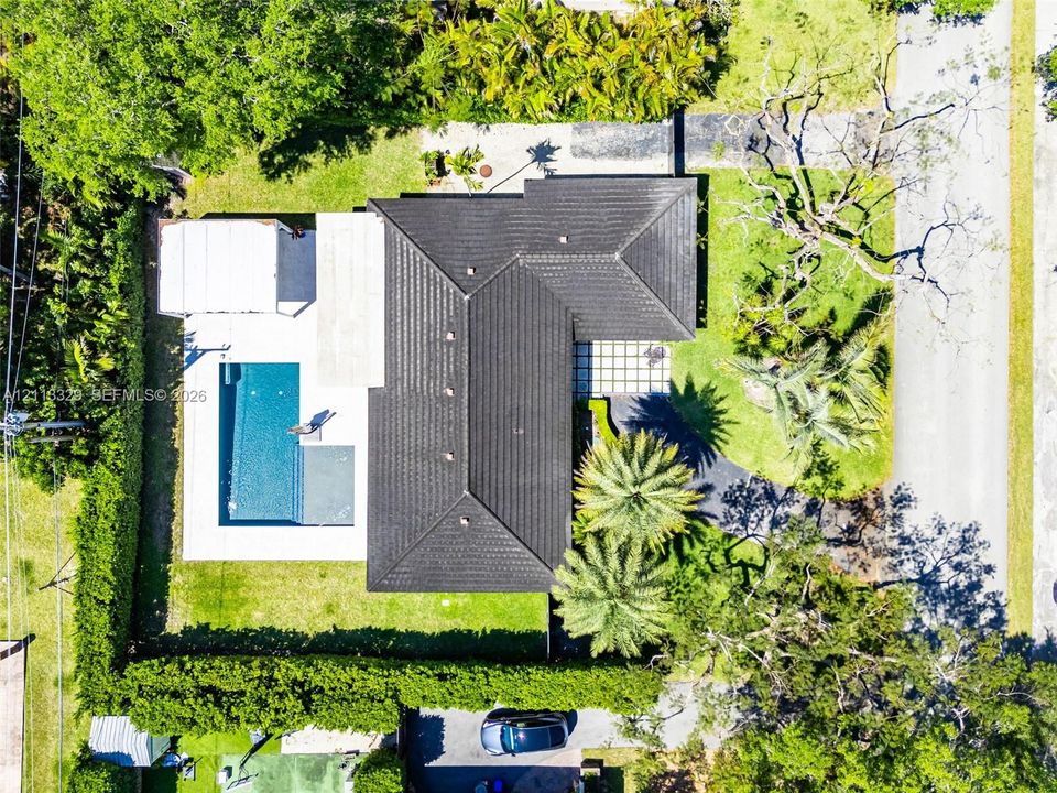Aerial perspective of a property featuring a dark-tiled roof, a rectangular swimming pool, concrete patio space, and mature landscaping
