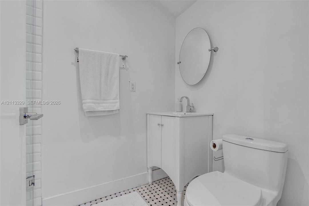 White vanity with a square sink, chrome faucet, oval wall-mounted mirror, and black-and-white mosaic tile flooring