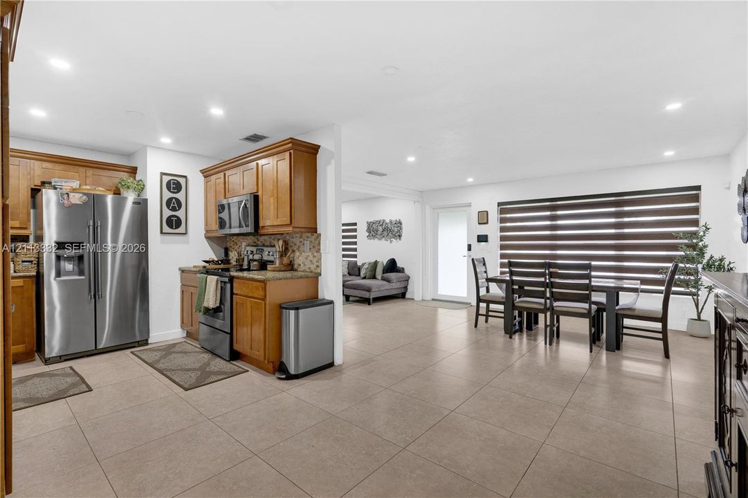 Kitchen featuring wood cabinetry, stone countertops, stainless steel appliances, recessed lighting, and large-format tile flooring