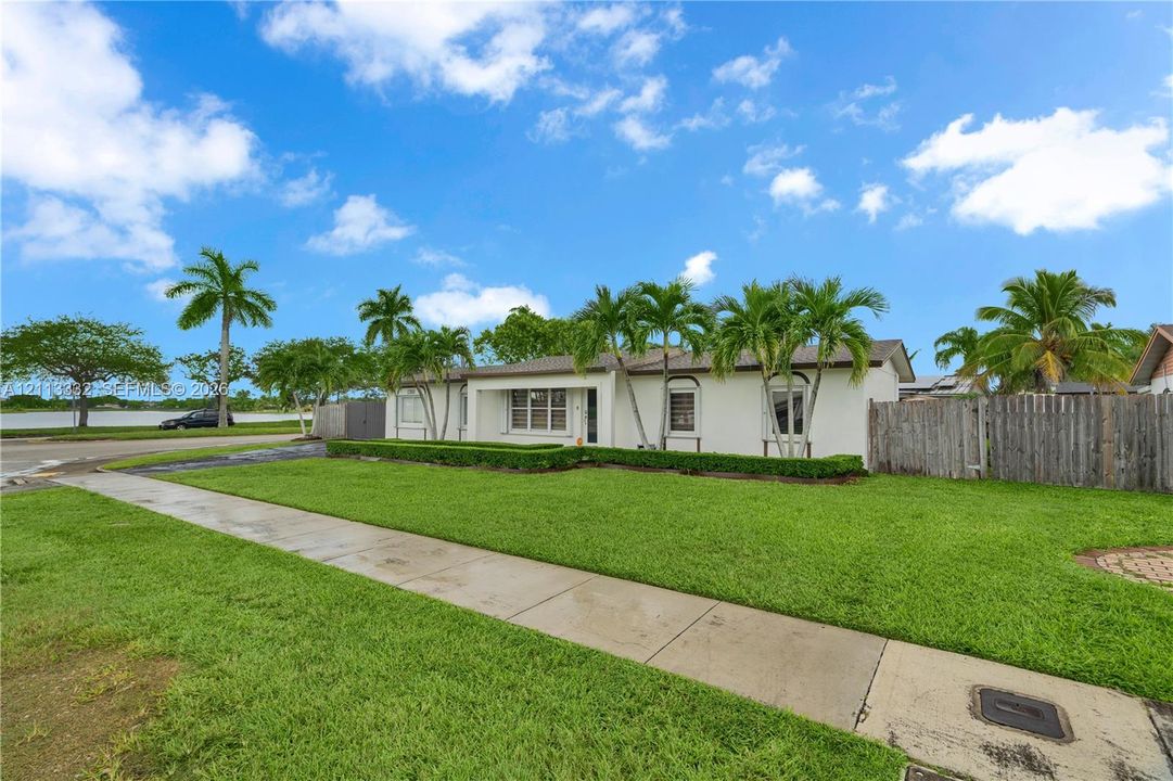 Single-story residence featuring a smooth stucco exterior, manicured lawn, established landscaping, and a wood privacy fence
