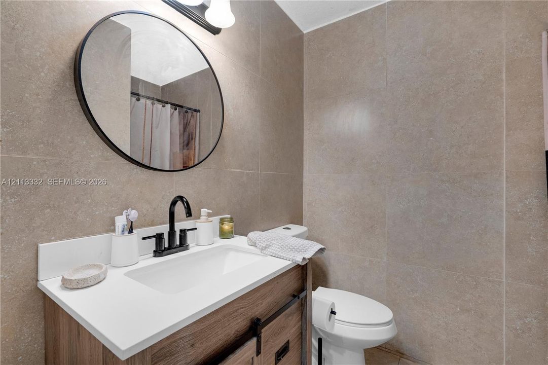 Bathroom featuring a vanity with a white countertop and wood-finish cabinetry, an oval mirror with a matte black frame, a matte black faucet, and full-height stone-finish wall tile