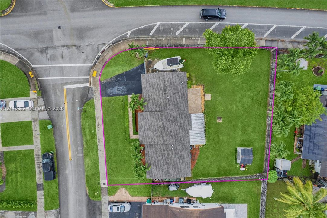 Corner lot featuring a large lawn, paved driveway, stone patio, and detached storage structure