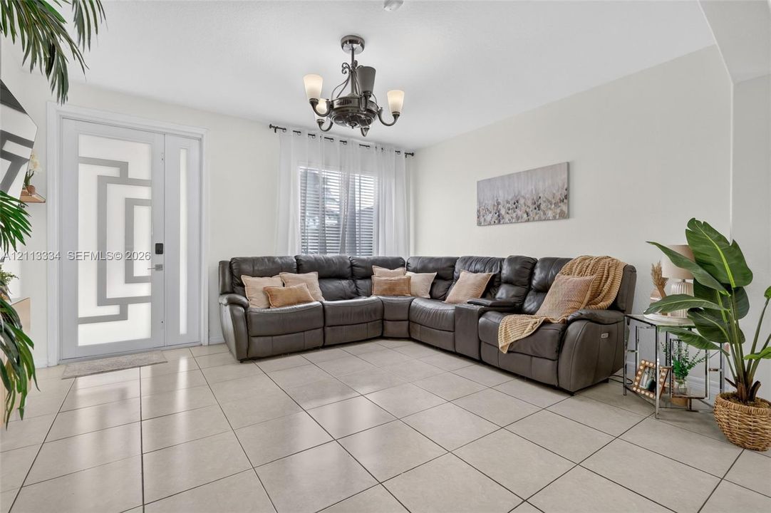 Neutral tile flooring, decorative front door with geometric glass inlay, and five-arm transitional chandelier