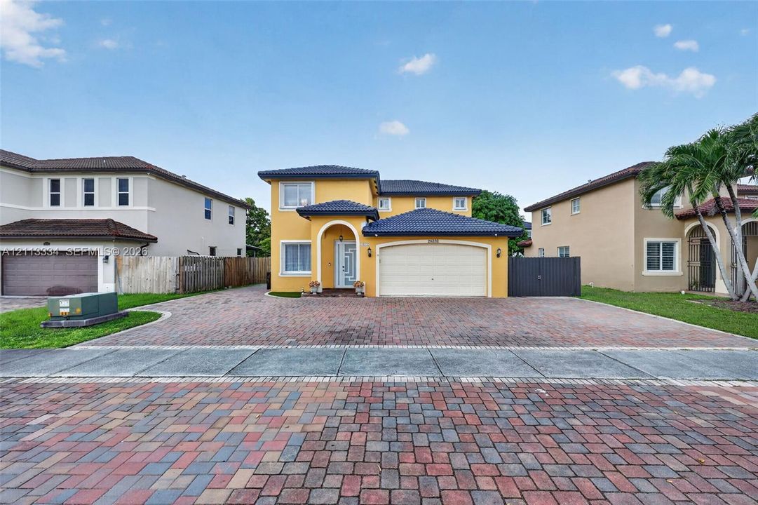 Two-story residence featuring a tile roof, stucco exterior, arched entryway, and a multi-car garage with a paver driveway