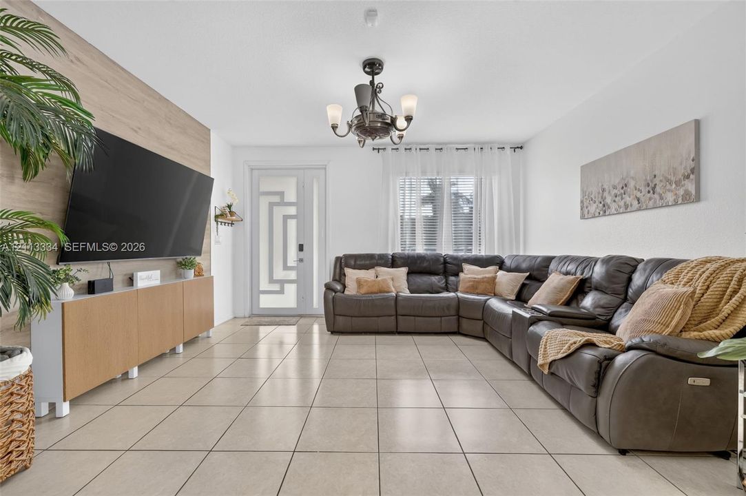 Living area featuring large-format tile flooring, a geometric paneled entry door, a floor-to-ceiling wood-finish accent wall, and a multi-arm chandelier