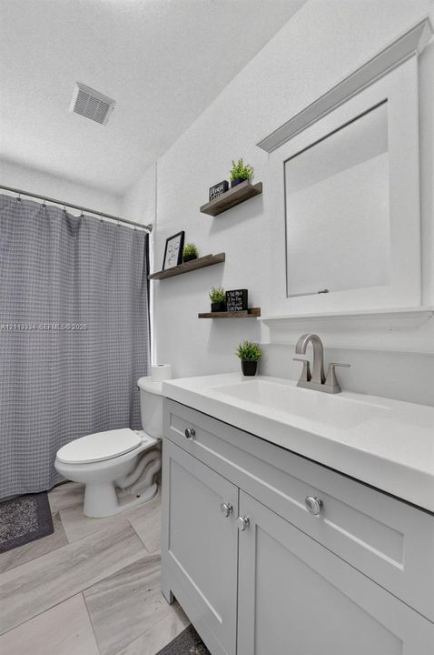 Bathroom featuring a vanity with a white integrated basin, brushed nickel faucet, light gray cabinetry, wall-mounted wood-finish floating shelving, and tile flooring