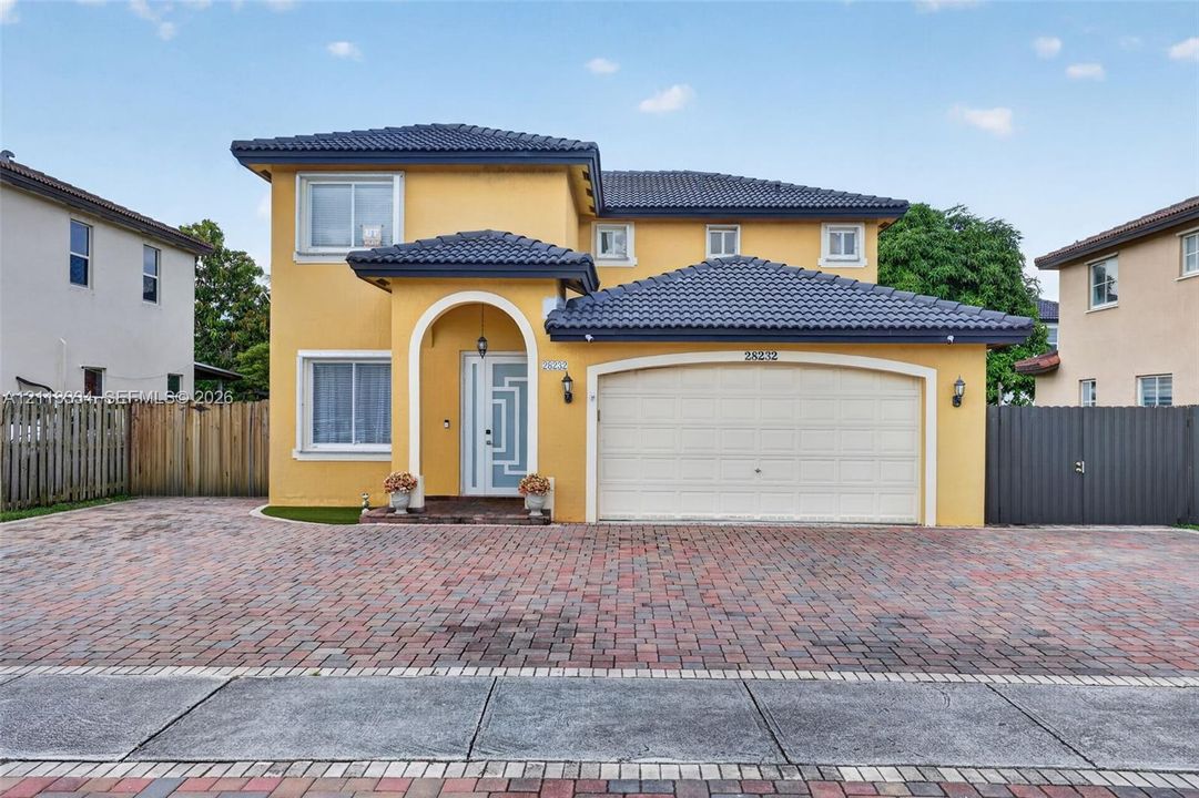 Two-story exterior featuring a tile roof, an arched entry, a geometric glass-panel front door, and a multi-car brick paver driveway