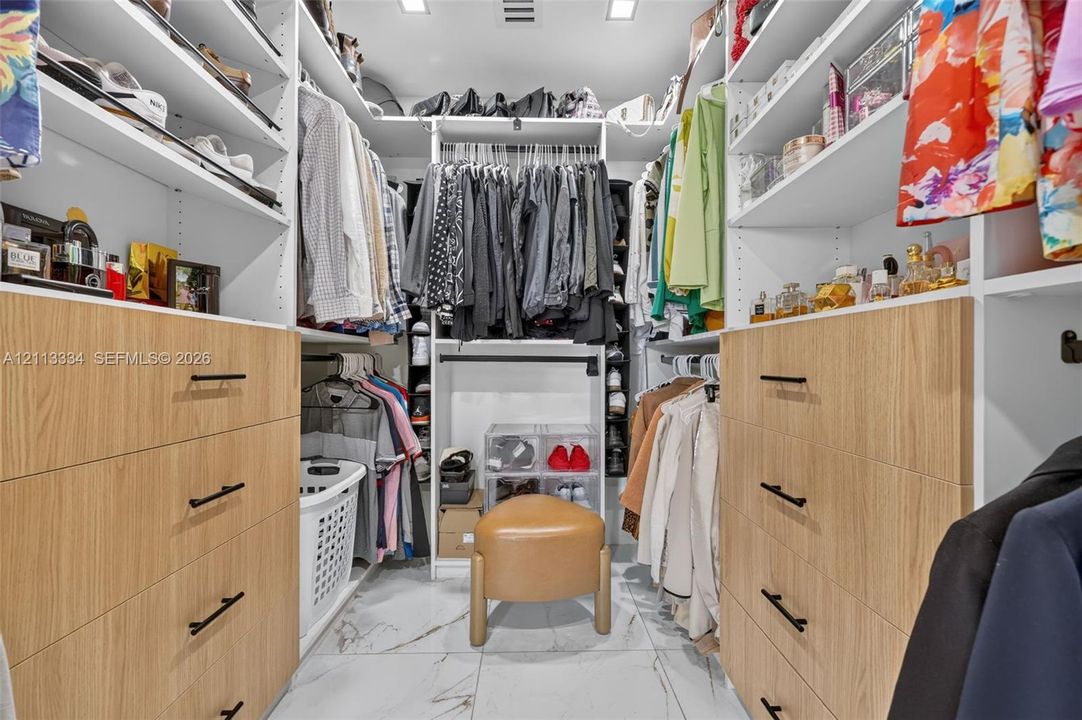 Custom walk-in closet featuring white built-in shelving, wood-finish cabinetry, matte black hardware, and stone-finish flooring