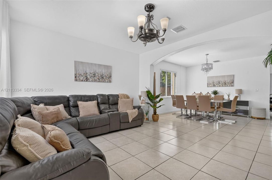 Neutral tile flooring, arched wall detailing, wrought-iron style multi-light chandelier, and decorative ceiling light fixtures