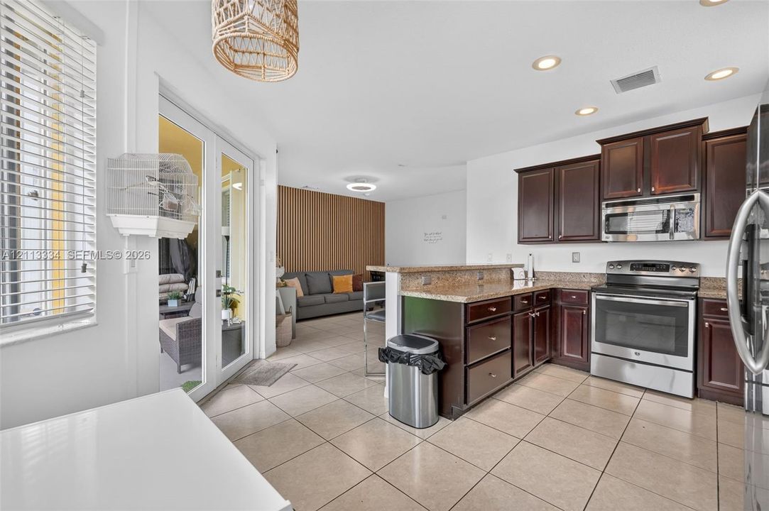 Kitchen featuring dark wood cabinetry, stone countertops, stainless steel appliances, tile flooring, and recessed lighting