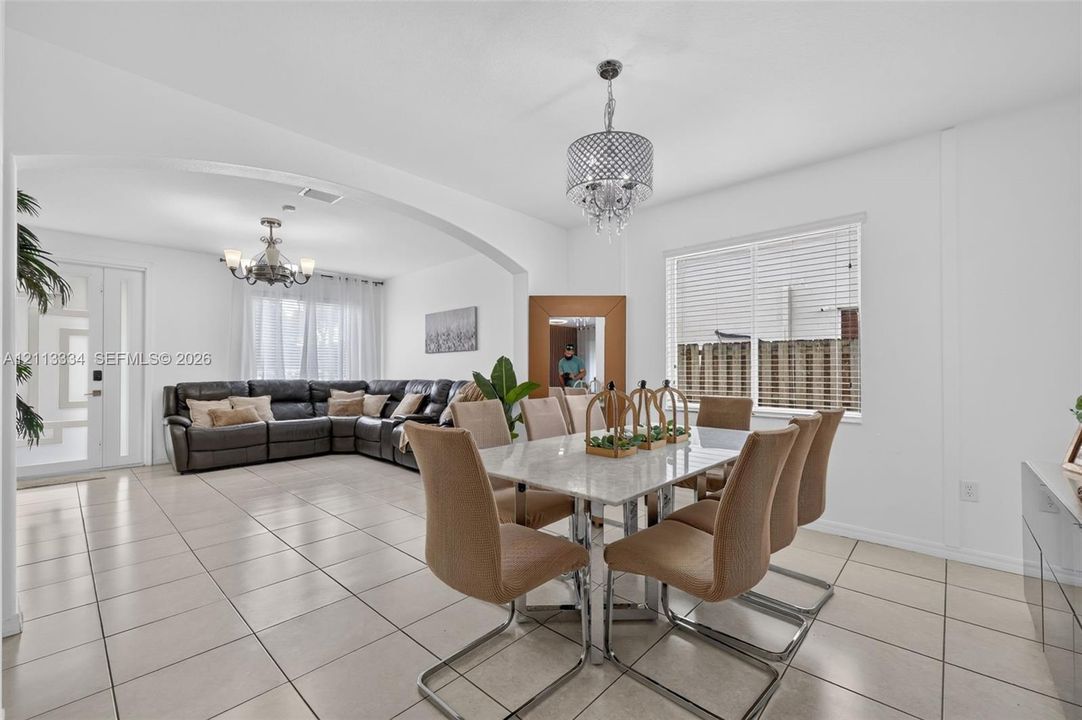 Open-concept interior featuring large-format ceramic tile flooring, arched architectural detailing, and two decorative crystal-style chandeliers