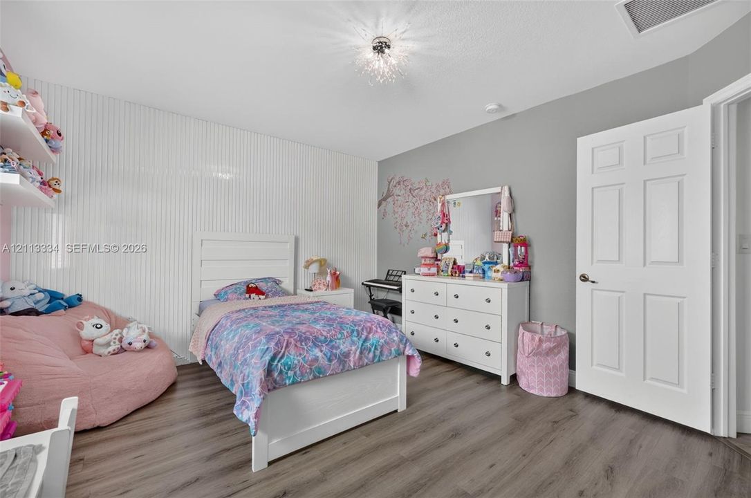 Bedroom featuring wood-finish flooring, textured vertical wall paneling, a six-panel interior door, and a decorative flush-mount ceiling fixture