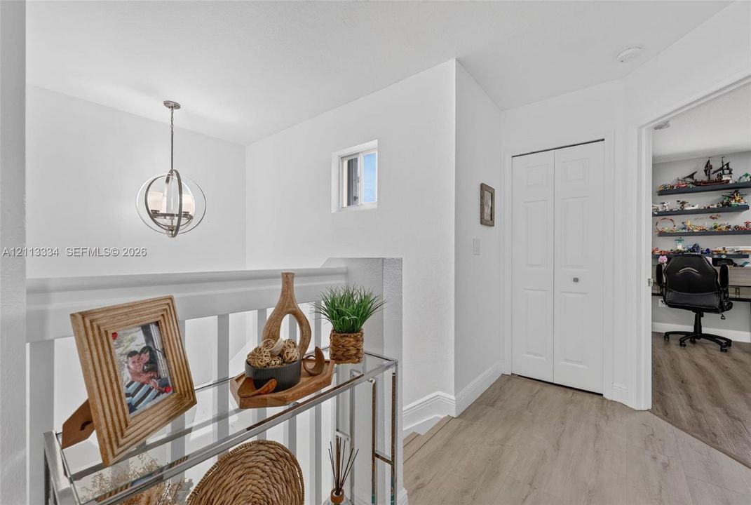 Hallway featuring wood-finish flooring, a contemporary spherical pendant light, a white bifold closet door, and a white baluster railing