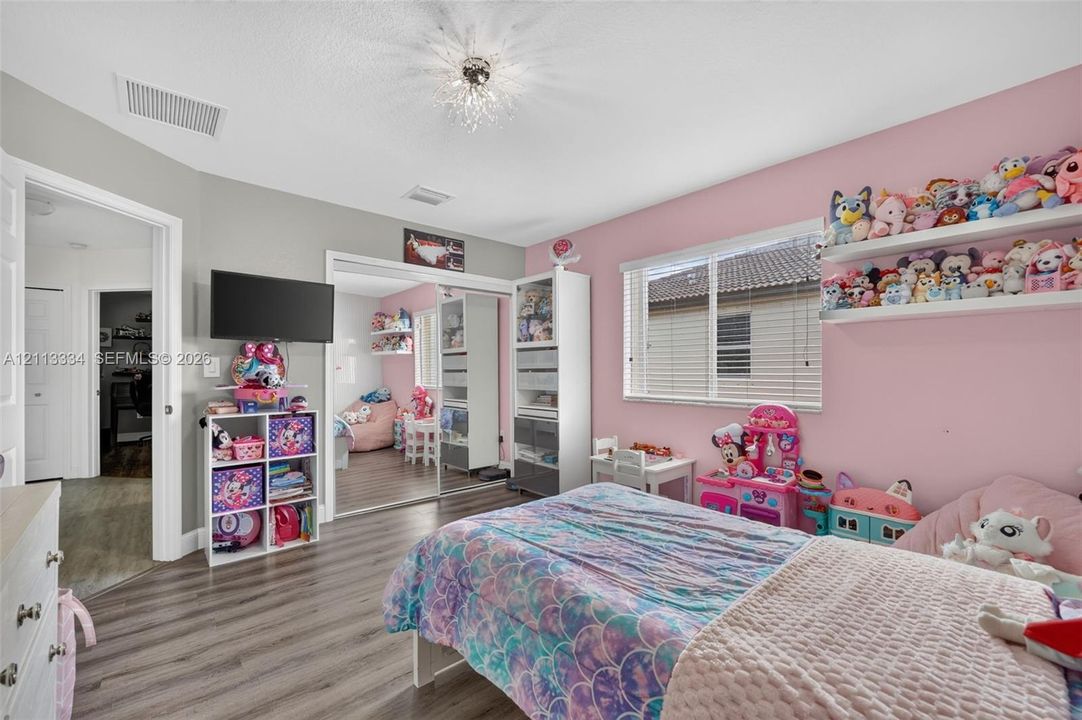 Bedroom featuring wood-finish flooring, mirrored sliding closet doors, a horizontal window with blinds, and an architectural starburst flush-mount ceiling light