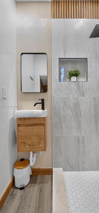 Wall-mounted wood-finish vanity with a rectangular sink, matte black faucet, rectangular mirror with a black frame, floor-to-ceiling stone-look wall tiling, and hexagonal floor tiles