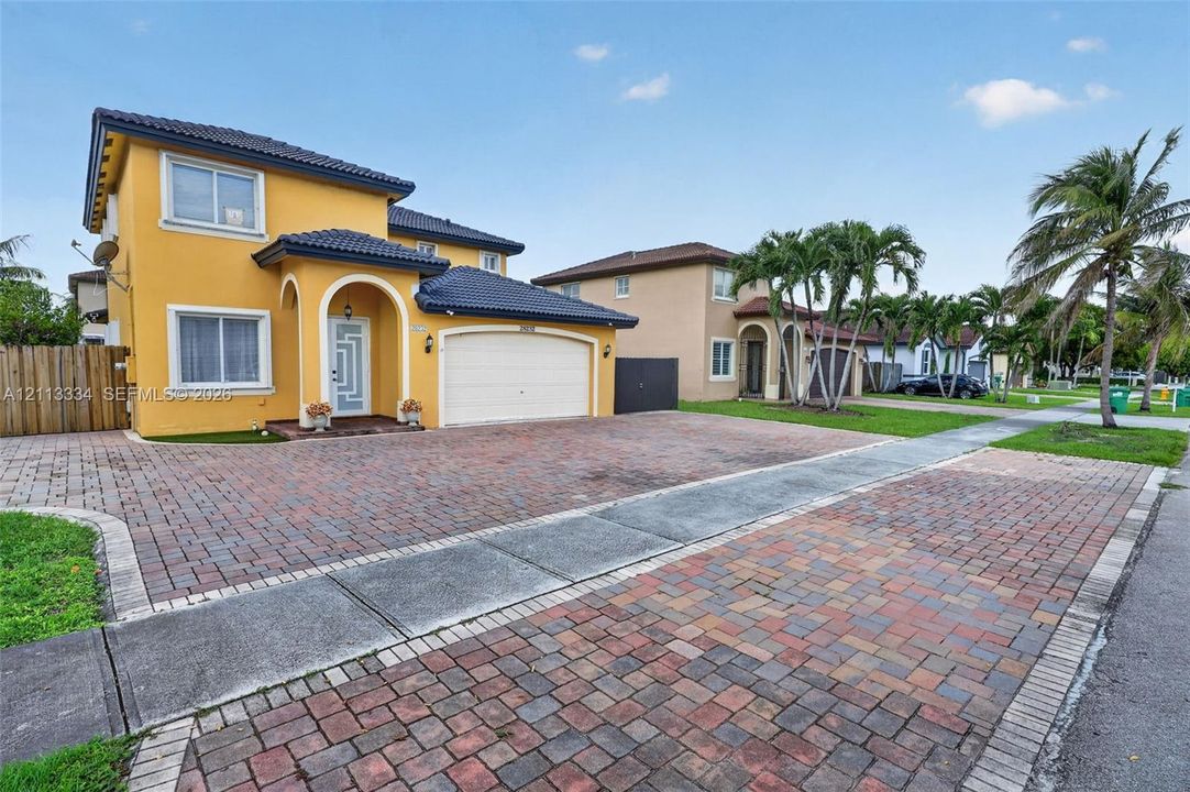 Two-story residence featuring a tile roof, decorative arched entryway, and extensive paver driveway