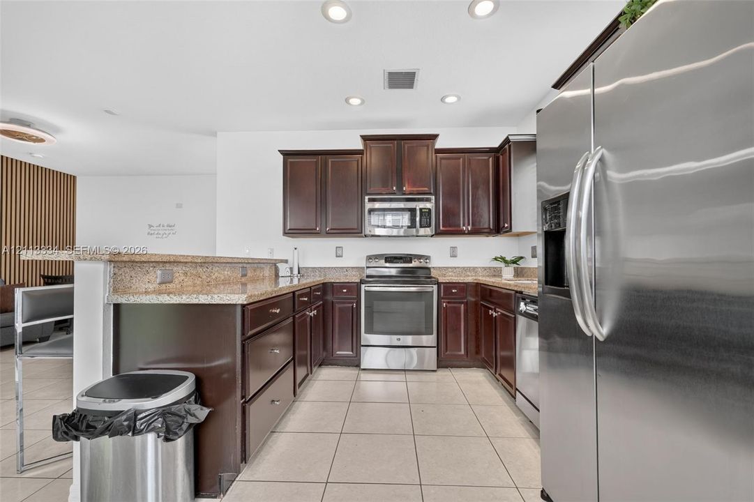Kitchen featuring dark-toned wood cabinetry, stone countertops, stainless steel appliances, and ceramic tile flooring