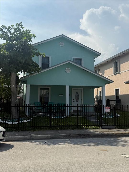 Two-story residence featuring a covered front porch, white support columns, dual-gabled roofline, and metal perimeter fencing