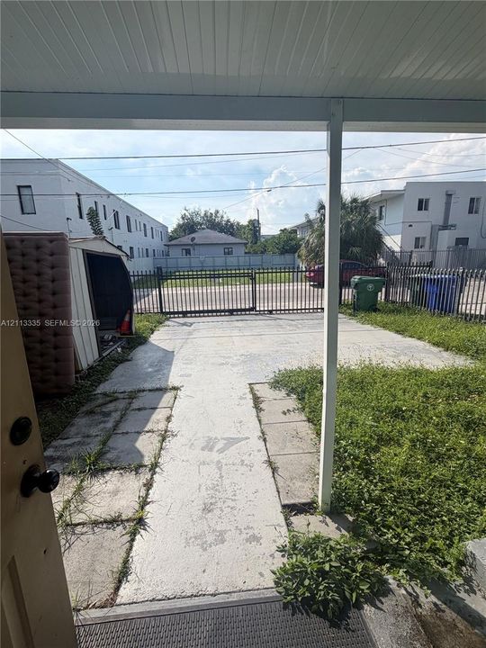 Covered porch entry featuring a concrete parking pad, metal security fencing, and gated access