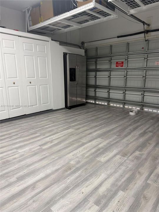Garage area featuring wood-finish flooring, built-in white dual-panel closet doors, stainless steel refrigerator, and overhead wire storage shelving