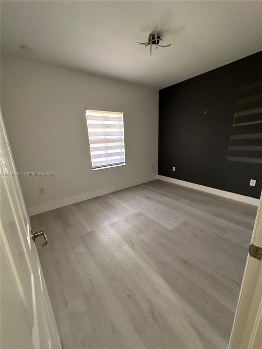 Interior room featuring wood-finish flooring, a charcoal accent wall, and a window with zebra-style light-filtering shades