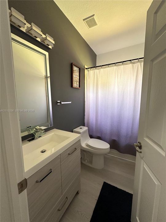 Bathroom featuring a wood-finish vanity with a rectangular sink, integrated mirror with light fixture, high-profile toilet, and wood-finish flooring