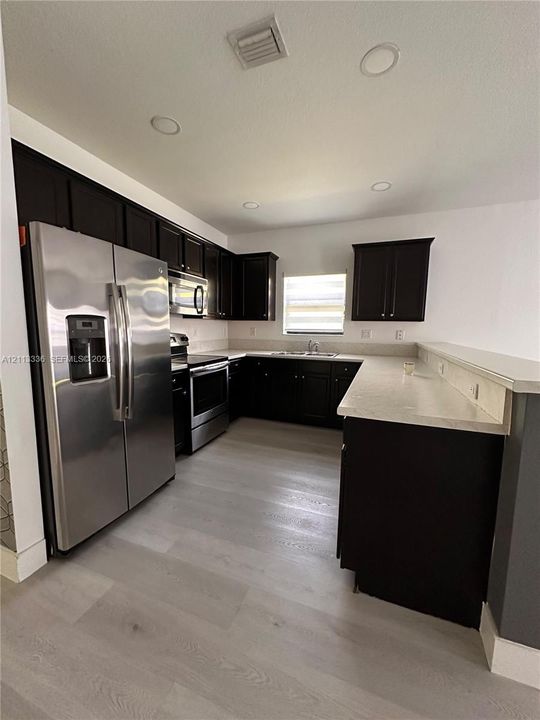 Kitchen featuring dark-finish cabinetry, light-toned stone-style countertops, stainless steel appliances, and wood-finish flooring