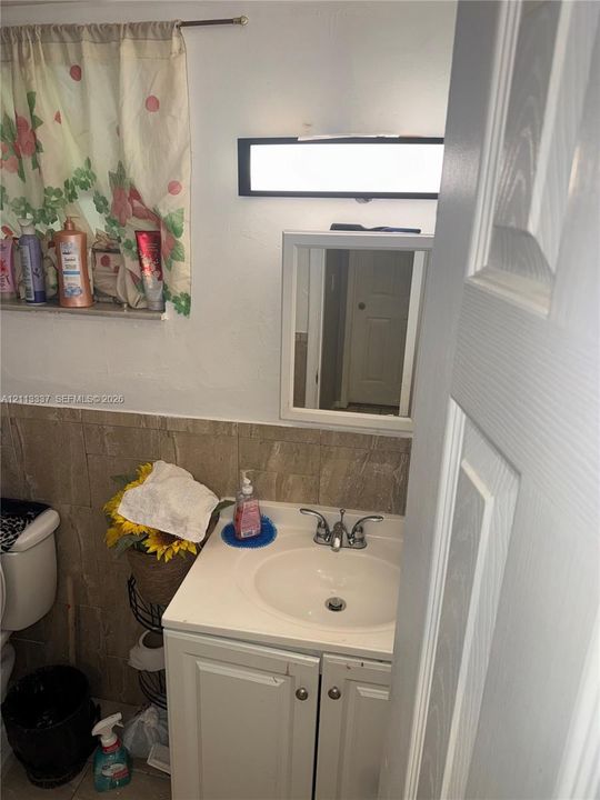 Bathroom featuring a white vanity cabinet, integrated sink, dual-handle faucet, rectangular medicine cabinet, and horizontal wall-mounted light fixture above tile wainscoting