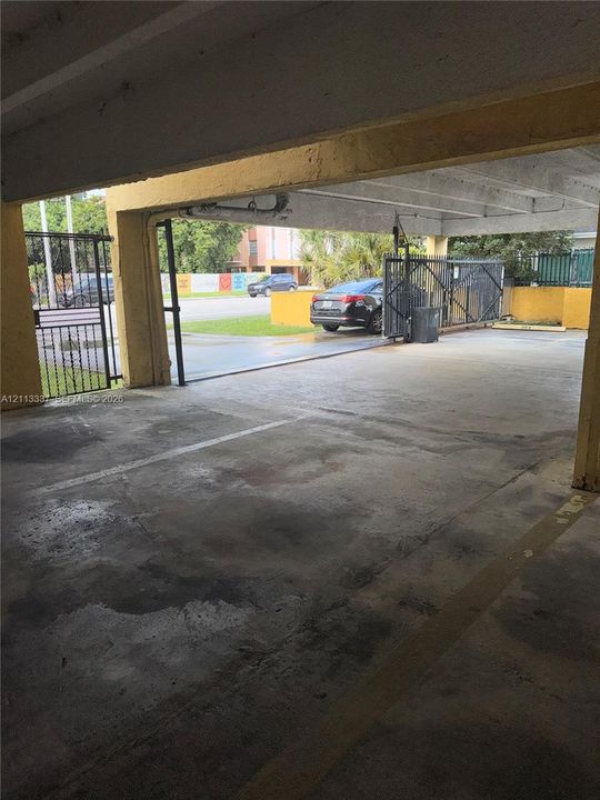 Covered parking area featuring concrete flooring, exposed structural beams, and a gated perimeter entry