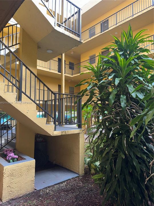 Multi-level exterior structure featuring open-air walkways, black metal railings, a stucco finish, and integrated planter boxes