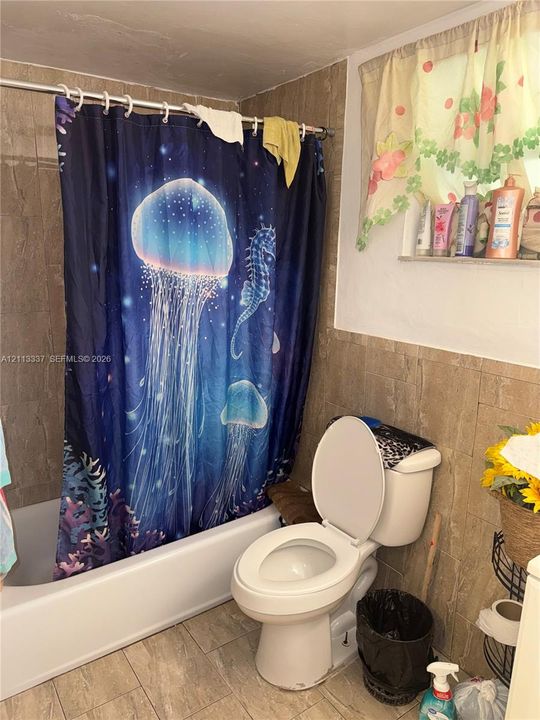 Bathroom featuring a standard white bathtub, ceramic tile wall surround, stone-finish floor tile, and a recessed wall niche