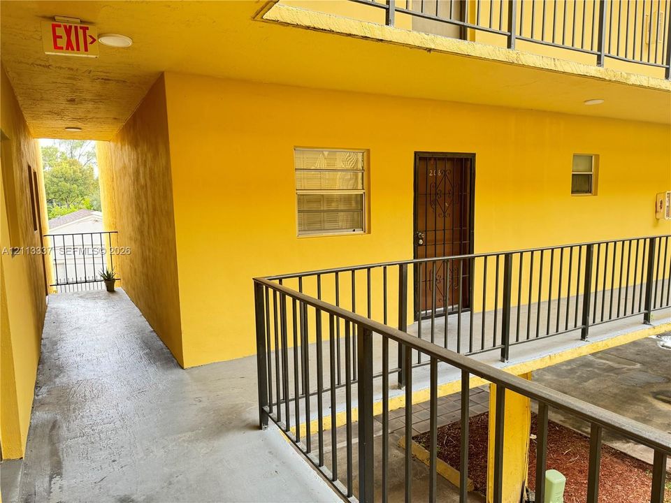 Exterior walkway featuring a concrete floor, dark metal railing, and a secure metal screen door