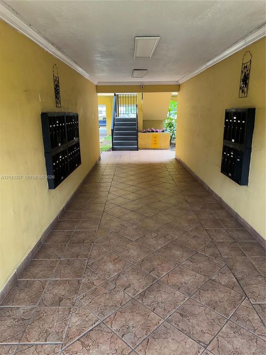 Covered exterior corridor featuring diamond-patterned stone tile flooring and dual wall-mounted metal mail centers