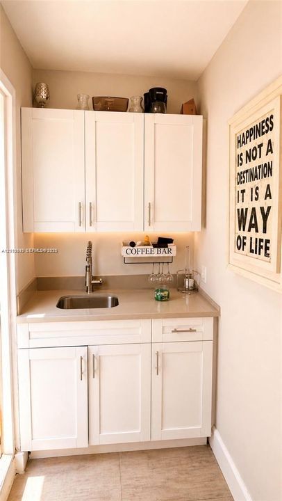 Built-in white cabinetry featuring shaker-style doors, matte-finish countertop, integrated stainless steel sink, gooseneck faucet, and under-cabinet lighting
