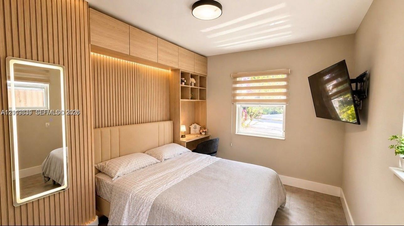 Slatted wood wall paneling with integrated accent lighting, custom built-in cabinetry featuring shelving and a desk surface, neutral wall finishes, and an illuminated rectangular wall mirror