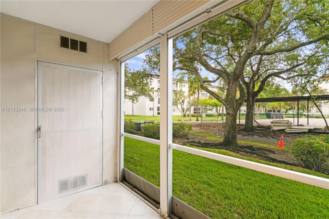 Enclosed patio featuring light-toned tile flooring, white-framed screening, and vertical blinds