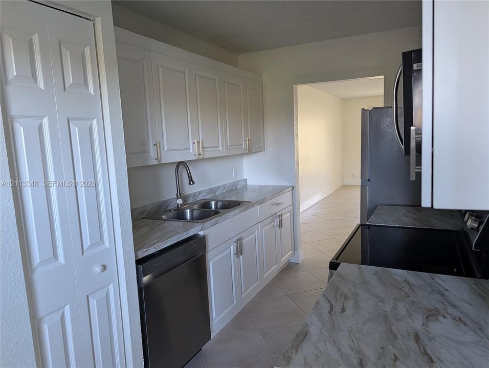 Kitchen featuring white cabinetry with brushed metal hardware, stone-patterned countertops, stainless steel appliances, and a dual-basin sink with a high-arch faucet