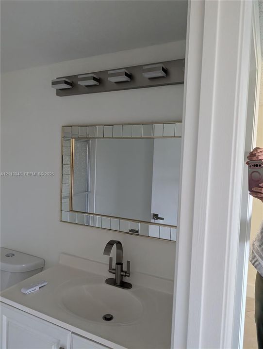 Wall-mounted vanity mirror with a decorative mosaic tile frame, four-light brushed metal vanity fixture, and a high-arch metal faucet